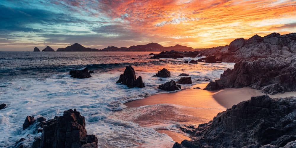 Dramatic sunset in Cabo San Lucas with a view of Land's End at the horizon.