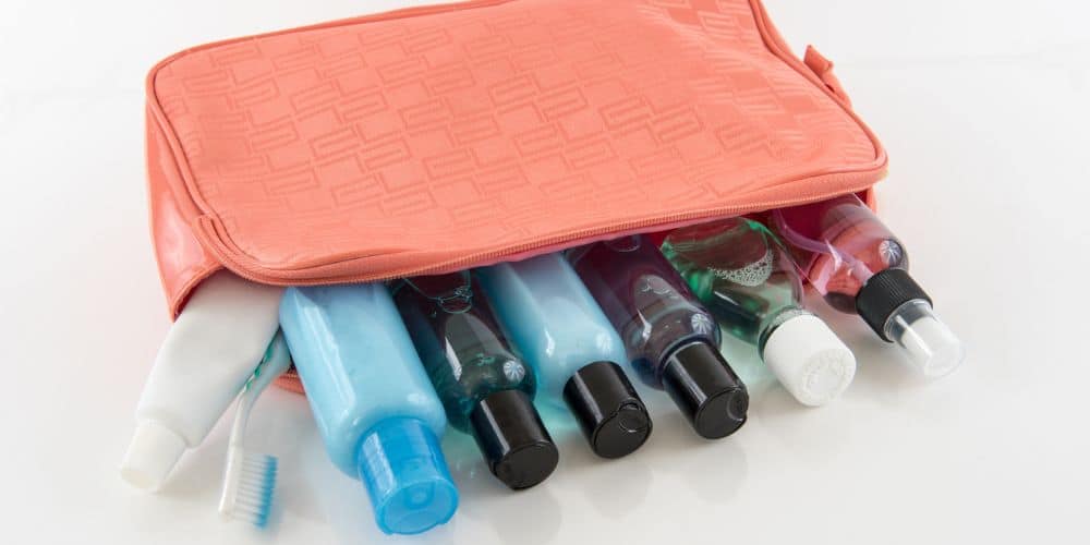 A travel toiletry bag with an assortment of travelsized hygiene products like shampoo, conditioner, and lotion bottles, alongside a toothbrush, laid out on a white surface.
