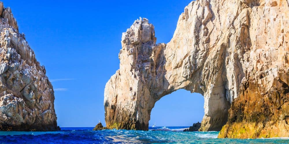 The natural rock formation known as The Arch of Cabo San Lucas stands majestically in the sea, with a clear blue sky above. 